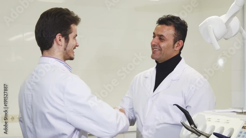 Cheerful handsome mature male dentist shaking hands with his younger colleague at the dental clinic partnership success medical team healthcare achiving doctors dentistry hospital. photo