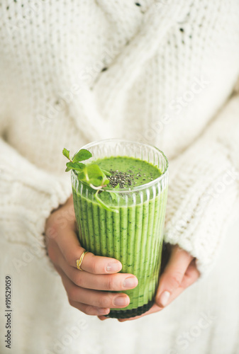 Matcha green vegan smoothie with chia seeds and mint in glass in hands of female wearing white sweater. Clean eating, detox, alkaline diet, weight loss concept