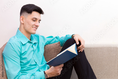 Portrait of a smiling young man in a green shirt reading a book