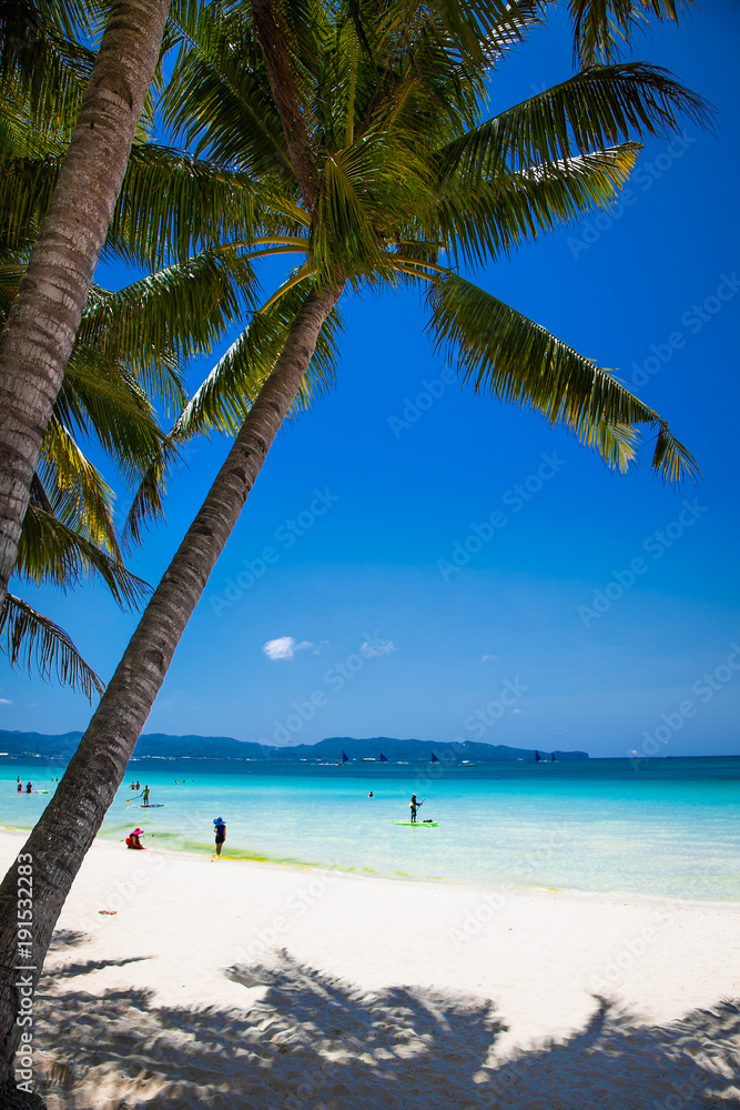 Tropical vacation on white sand beach with sun, blue sky and palm trees. White beach at Boracay, Philippines.