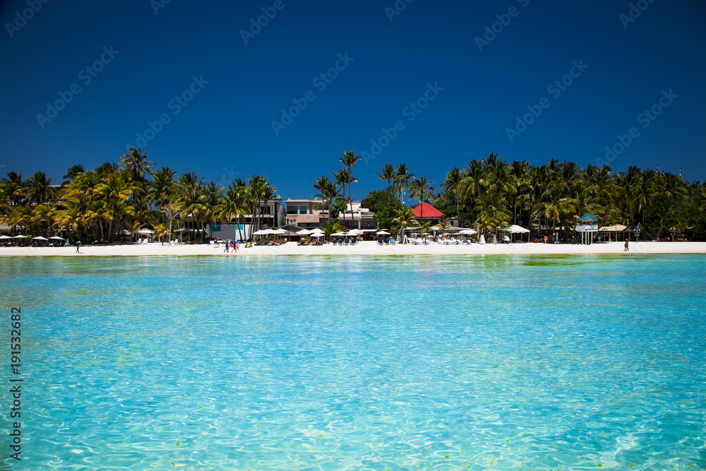 Tropical vacation on white sand beach with sun, blue sky and palm trees. White beach at Boracay, Philippines.
