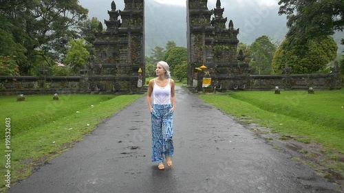 Slow motion shot of woman strolling on a road outside a candi bentar in Indonesia photo