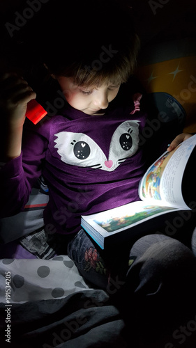 bambina che legge al buio con la torcia photo