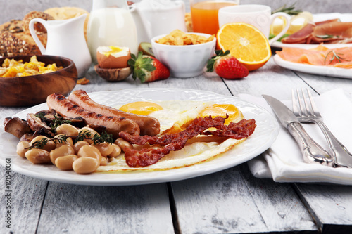 Traditional full English breakfast with fried eggs, sausages, beans, mushroomsand bacon on wooden background