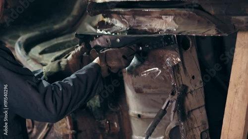 Male workeres in workclothes stand beside the car's bottom surface. One workman adjusts metal detail to car construction using coupling nut. photo