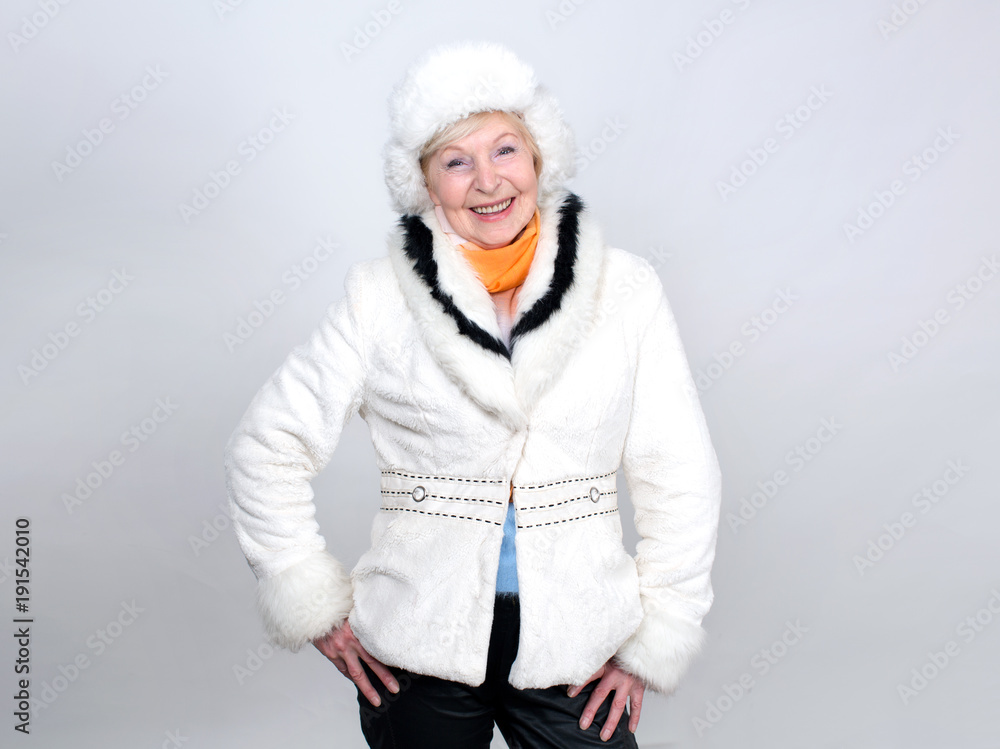 Happy senior woman with a smile on her face. Smiling woman in warm winter clothes standing on a light background. Happy senior woman with a smile on her face. Smiling woman in warm winter clothes standing on a light background.