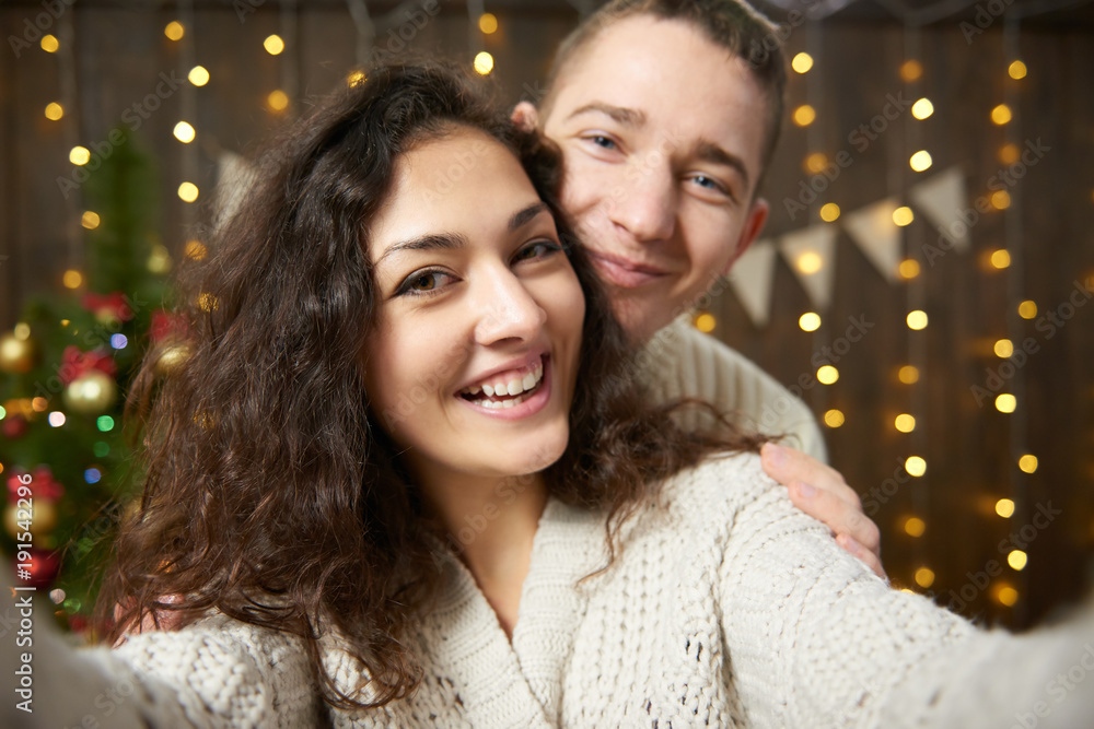 Happy couple taking selfie and having fun in christmas decoration. Dark wooden interior with lights. Romantic evening and love concept. New year holiday. Happy couple taking selfie and having fun in christmas decoration. Dark wooden interior with lights. Romantic evening and love concept. New year holiday.