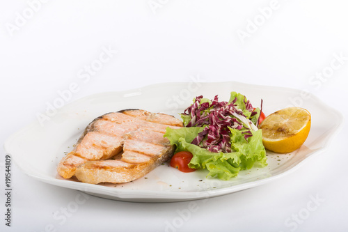 fried salmon steak with salad and lemon on a white plate isolate