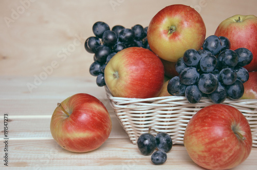 Apples and grapes in a wicker basket on wooden table