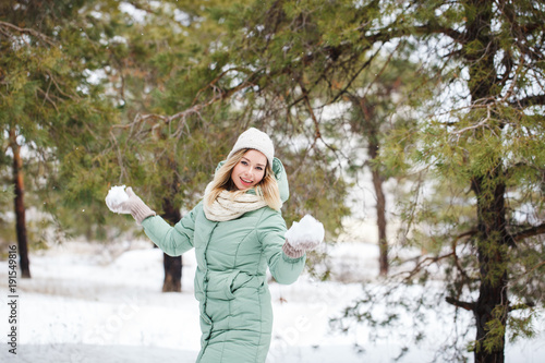 Attractive beautiful girl holds snow in hands and smiles. Portrait of a slender cute girl on a winter background, looking at the camera and smiling. Space for text