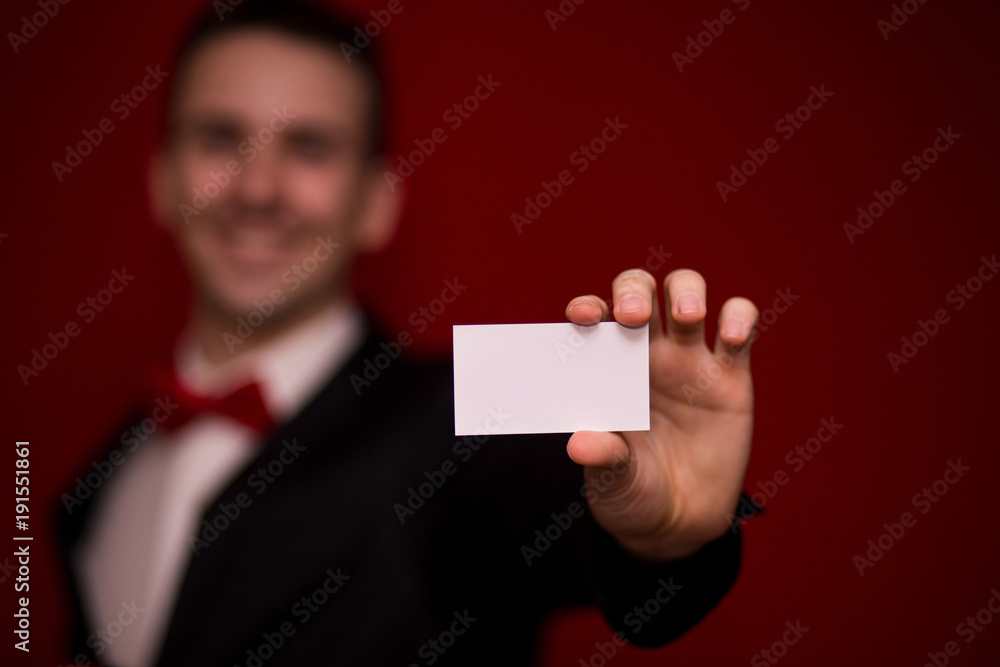 Stylish man in suit hold white business card on red background, focus on business card. Business concept Stylish man in suit hold white business card on red background, focus on business card. Business concept