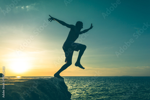 Man jumping over a cliff into the sea on sunset in Koh Phangan island, Thailand. Vintage effect. Dare, fearless concept. Two out of three series photo