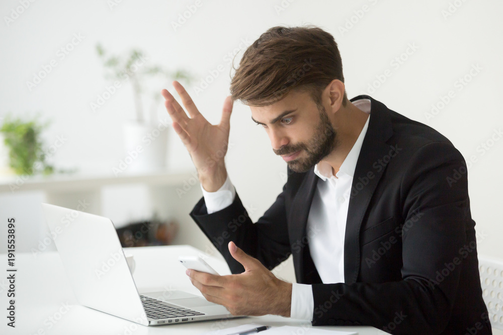 Angry businessman stressed about smartphone problem at workplace, frustrated executive feeling indignant annoyed about phone call, broken not working cell, received spam bad news in mobile message Angry businessman stressed about smartphone problem at workplace, frustrated executive feeling indignant annoyed about phone call, broken not working cell, received spam bad news in mobile message