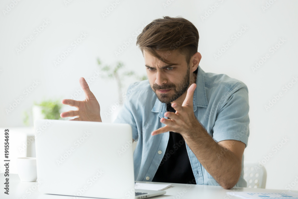 Frustrated angry entrepreneur outraged by laptop problem, furious mad man  using computer looking at screen raging after pc software crash error,  annoyed guy frustrated disagree with fake online news Stock Photo