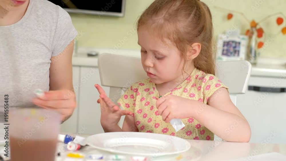 Happy family, mother and little daughter paint with paint on white plates Happy family, mother and little daughter paint with paint on white plates