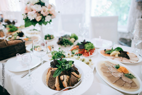 Wedding reception white table arrangement, floral centerpiece decoration, food. Catering service.