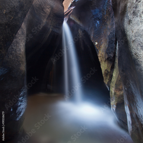 A small waterfall between two boulders in a slot canyon in Zion National park