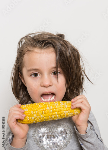 Indoor close-up portrait of young girl  eating corn-cob isolated on a white background.