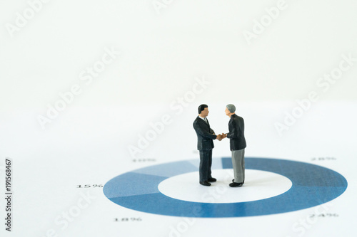Agreement or deal for business success, miniature executive businessmen handshaking on printed performance pie chart or graph with copy space and seamless white background