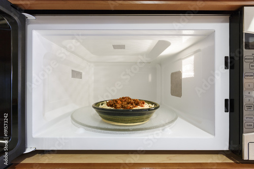 Kitchen home appliances cooking reheating plate bowl dish food meal dinner of cooked spaghetti pasta with Bolognese tomato meat sauce in microwave oven photo
