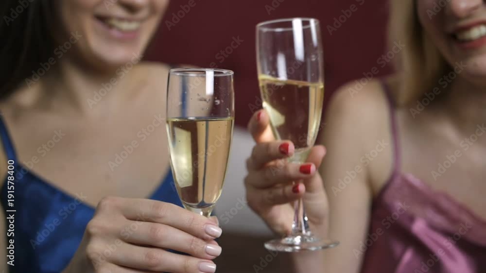 Close-up of female best friends in lingerie chatting, laughing and toasting champagne together in bedroom. Happy positive women clinking champagne glasses and drinking. Slow motion. Dolly shot Close-up of female best friends in lingerie chatting, laughing and toasting champagne together in bedroom. Happy positive women clinking champagne glasses and drinking. Slow motion. Dolly shot