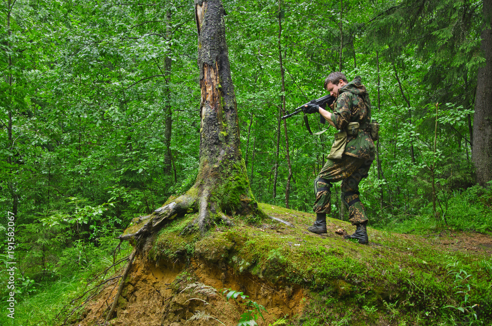 soldier aims and shoots standing in a fighting stand on a hill in the forest