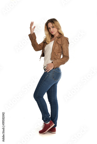 full length portrait of blonde girl wearing simple brown jacket and jeans, standing pose on white studio background.