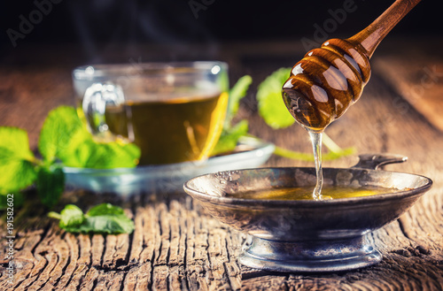 Honey. Honey and honey dipper on rustic oak table. Hot herb tea in the background photo