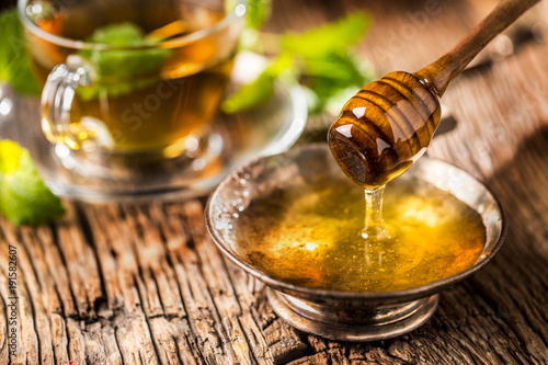 Honey. Honey and honey dipper on rustic oak table. Hot herb tea in the background