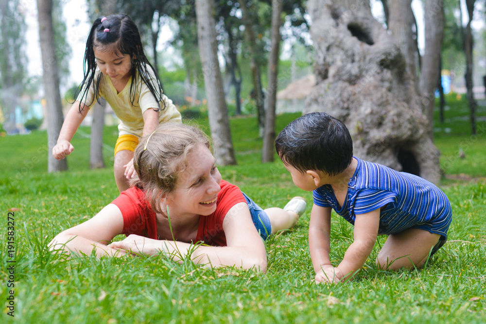 Happy biracial family in the summer park - caucasian mother with her latin children laying on the grass.