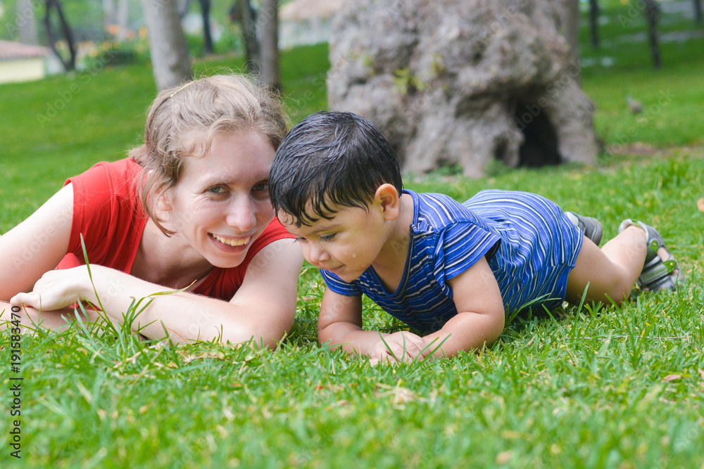 Happy biracial family in the summer park - caucasian mother with her latin son laying on the grass. Happy biracial family in the summer park - caucasian mother with her latin son laying on the grass.