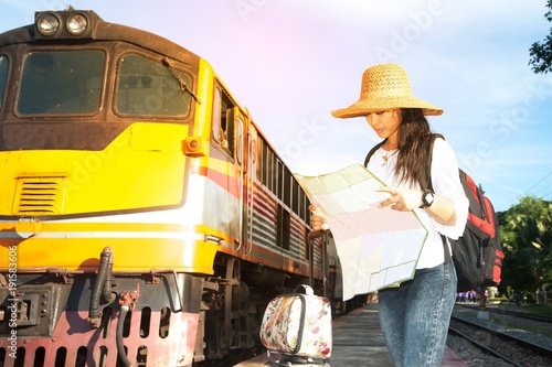 Pretty Asian traveler backpacker female looking map and waiting train at railway station in Thailand.