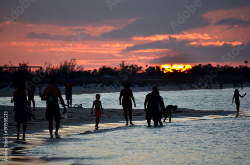 Dramatic sunset over a tropical beach in the Caribbean  Cayo Coco  Cuba . Silhouettes of people walking on the shore. 