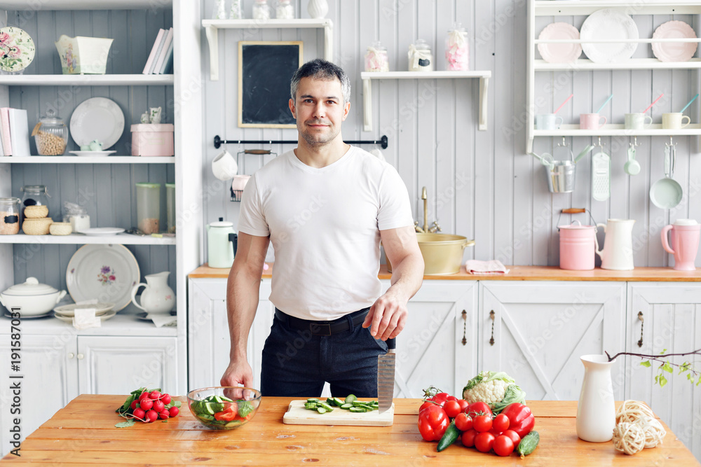 Portrait of handsome smiling man at kitchen. cooking and home concept - close up of male hand chopping cucumber on cutting board with sharp knife Portrait of handsome smiling man at kitchen. cooking and home concept - close up of male hand chopping cucumber on cutting board with sharp knife