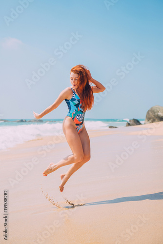 happy young red-haired woman jumping on a tropical beach on a sunny afternoon