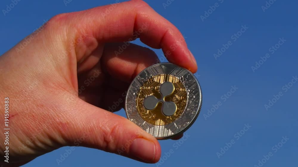 Female hand holds a bitcoin coin in the hands against a blue sky Female hand holds a bitcoin coin in the hands against a blue sky