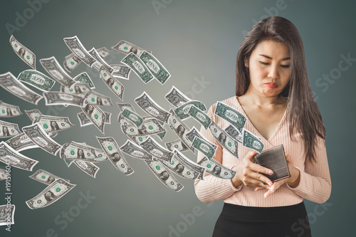 unhappy and poor Asian woman holding  purse having problem with money flying away, over spending concept background