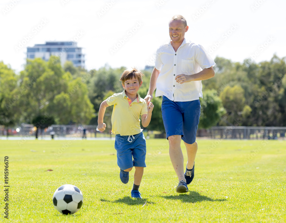 young happy father and excited little 7 or 8 years old son playing together soccer football on city park garden running on grass kicking the ball young happy father and excited little 7 or 8 years old son playing together soccer football on city park garden running on grass kicking the ball