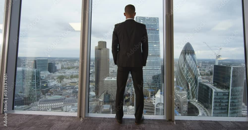 4K View from behind of African American businessman looking out at the view from London city office. 4K View from behind of African American businessman looking out at the view from London city office.