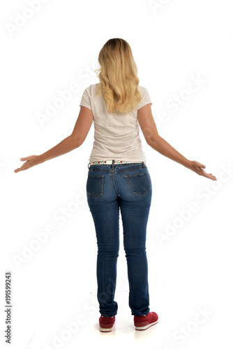 full length portrait of blonde lady wearing simple white shirt and jeans, standing pose isolated on white studio background.