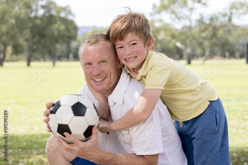 young happy father and excited 7 or 8 years old son playing together soccer football on city park garden posing sweet and loving holding the ball