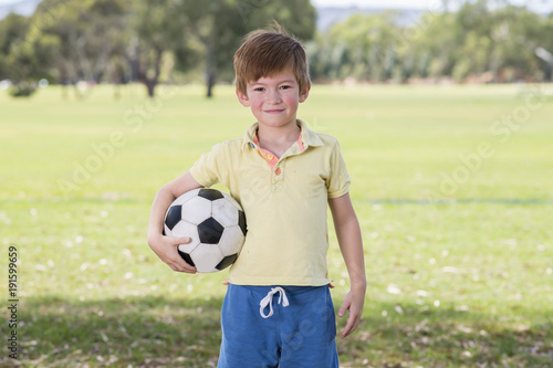 young little kid 7 or 8 years old enjoying happy playing football soccer at grass city park field posing smiling proud standing holding the ball © Wordley Calvo Stock