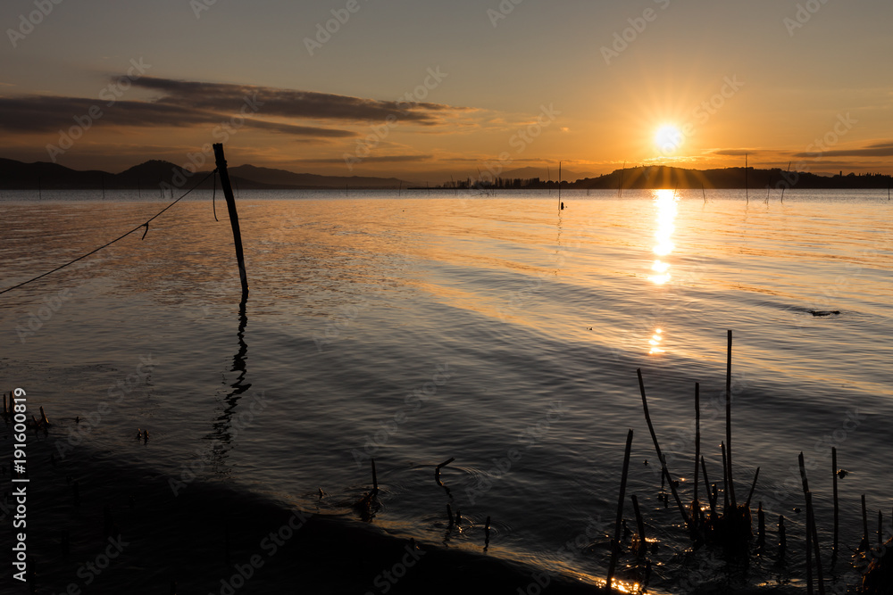 Beautiful sunset over Trasimeno lake (Umbria), with sun coming down behind an island and some fishing nets in the foreground