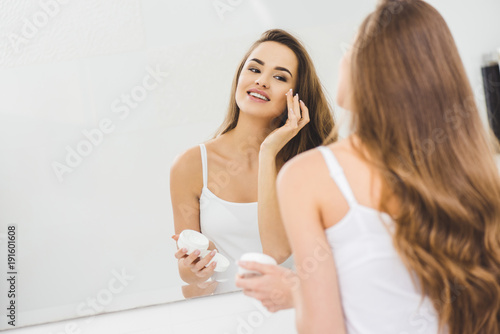 mirror reflection of beautiful woman applying face cream