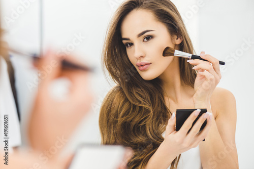 mirror reflection of beautiful young woman applying makeup
