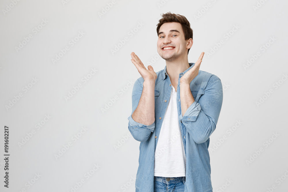 Studio portrait of young happy man with stylish haircut, smiling cheerfully while raising hands to clap, standing excited over gray background. Finally his girlfriend arriving back home Studio portrait of young happy man with stylish haircut, smiling cheerfully while raising hands to clap, standing excited over gray background. Finally his girlfriend arriving back home