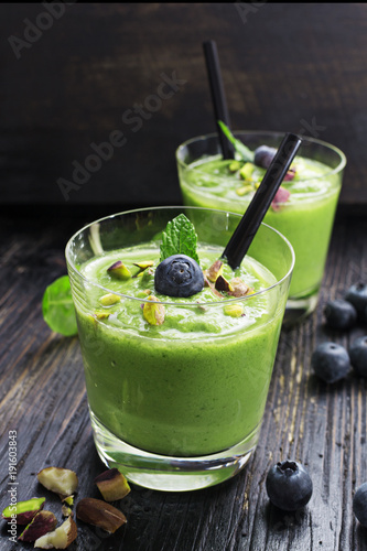 Smoothie with green spinach, pistachio on dark wooden board. Well being and weight loss concept.