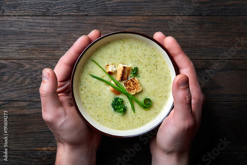Close up pictire of man's hands holding bowl with home made vegetable soup on the dark wooden background. photo
