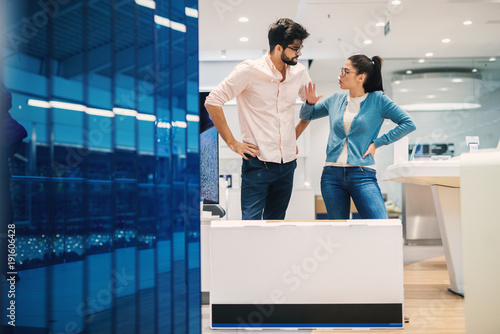 Photos Attractive hipster young couple arguing in the electronic shop with cartoon box in front with new electronics