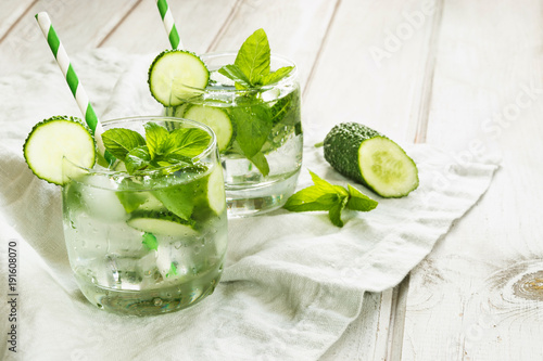 Summer refreshing detox cocktail. Water with cucumber,mint and ice in glass on a white wooden board. Rustic style.
